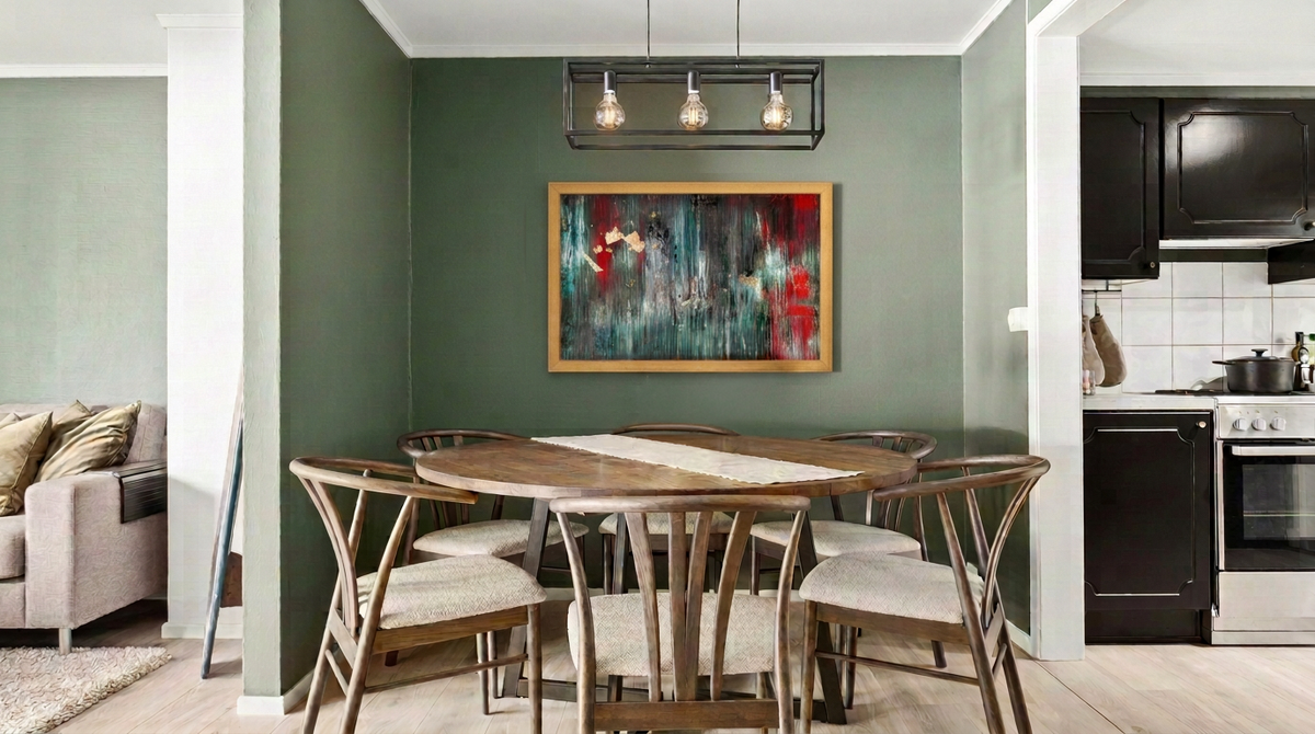 Gold picture frame with abstract art hanging on a green dining room wall above a round wood table